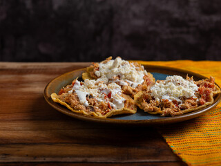 Tostadas with chicken tinga, cheese and cream on a plate on a wooden table. Typical Mexican food