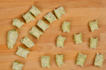 An overhead view of a cluster of raw potato and arugula gnocchi, irregularly arranged on a wooden surface