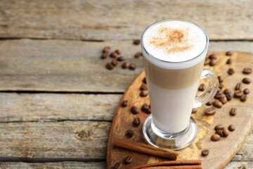 Tasty latte macchiato in glass cup, coffee beans and cinnamon on wooden table, closeup. Space for text