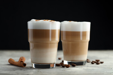Tasty latte macchiato in glasses, coffee beans and cinnamon on grey table, closeup
