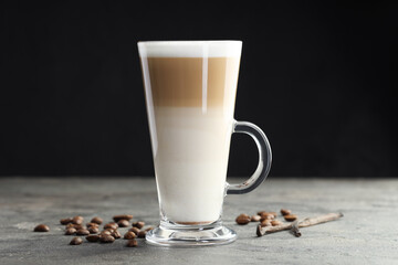 Tasty latte macchiato in glass cup, coffee beans and vanilla pods on grey table, closeup
