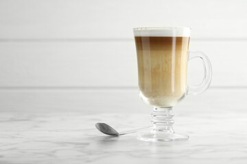 Tasty latte macchiato in glass cup on white marble table, closeup. Space for text