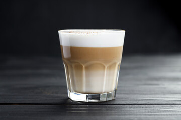 Tasty latte macchiato in glass on black wooden table, closeup