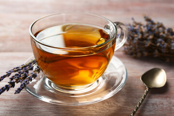 Aromatic lavender tea in glass cup, spoon and dry flowers on wooden table, closeup