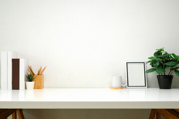 Modern workspace with books, a cup of coffee, blank picture frame, and a potted plant