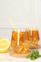 Refreshing iced tea with slices of lemon, mint and drinking straws on white marble table, closeup