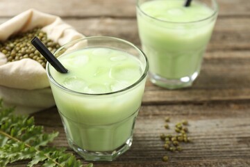 Fresh mung bean juice with ice in glasses, leaves and seeds on wooden table, closeup
