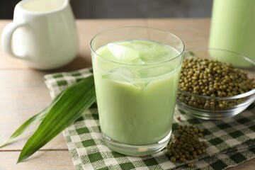 Fresh mung bean juice with ice in glass, leaves and seeds on wooden table, closeup