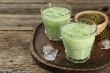 Fresh mung bean juice with ice in glasses and seeds on wooden table, closeup. Space for text