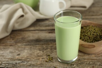 Fresh mung bean juice in glass and seeds on wooden table, closeup. Space for text