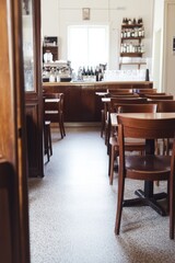 Fototapeta premium Cozy interior of a small cafe featuring wooden furniture and a sunlit bar area in a quiet urban setting