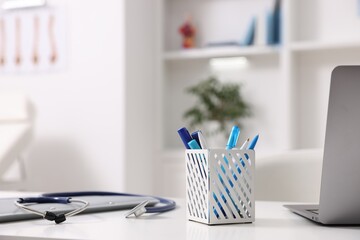 Laptop, stethoscope and folders on desk in medical office, closeup