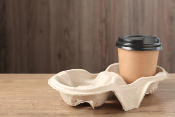 Paper coffee cup in cardboard holder on wooden table, closeup. Space for text