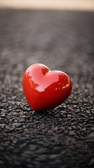 Fototapeta premium A glossy red heart-shaped object resting on a textured dark surface.