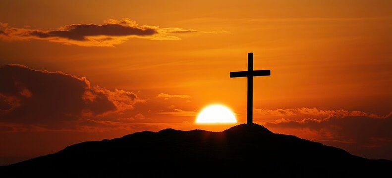 Silhouette of a cross atop a hill at sunset