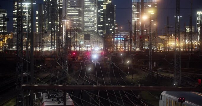 Zug f&auml;hrt unter Br&uuml;cke durch in den Frankfurter Hauptbahnhof bei Nacht mit Sicht auf die Skyline