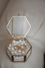A small box with a chain and two rings inside. The box is made of gold and has a white background