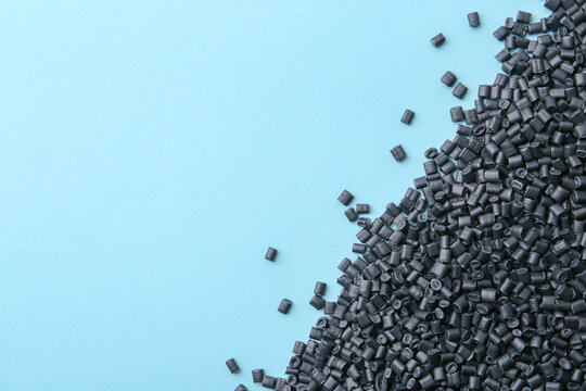 Pile of black plastic granules on light blue background, top view. Space for text