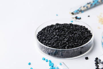 Colorful plastic granules in petri dish and test tubes on white background, closeup. Space for text