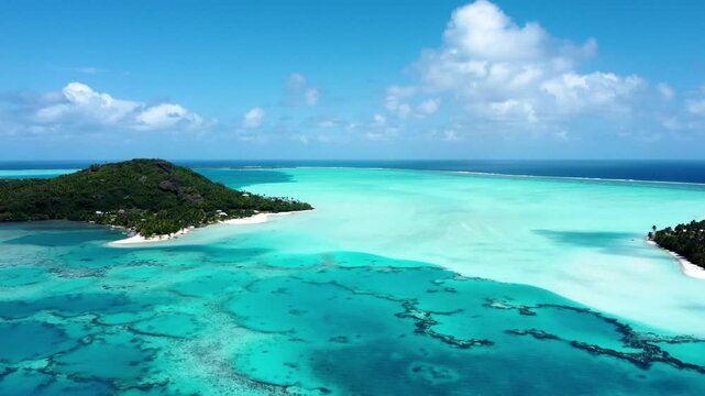 Drone view of a small green pacific tropical island with a lagoon, coral reef, white sand beach and blue shallow water on a sunny day in Maupiti, French Polynesia.