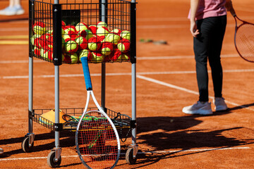 Basket cart filled colorful tennis balls Kids-training clay tennis court children playing training...