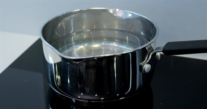 mid shot of putting a pan of water onto an induction hob and the water starting to boil then taking the pan away.