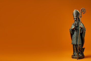 Fototapeta premium Saint Patrick bronze figurine with clover staff, Celtic harp and cross on orange background with copy space for text. Saint Patrick's day horizontal banner. Statue of Apostle of Ireland