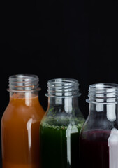 Close up of bottles of carrot, spinach and beetroot smoothies on a dark background. Healthy natural drinks