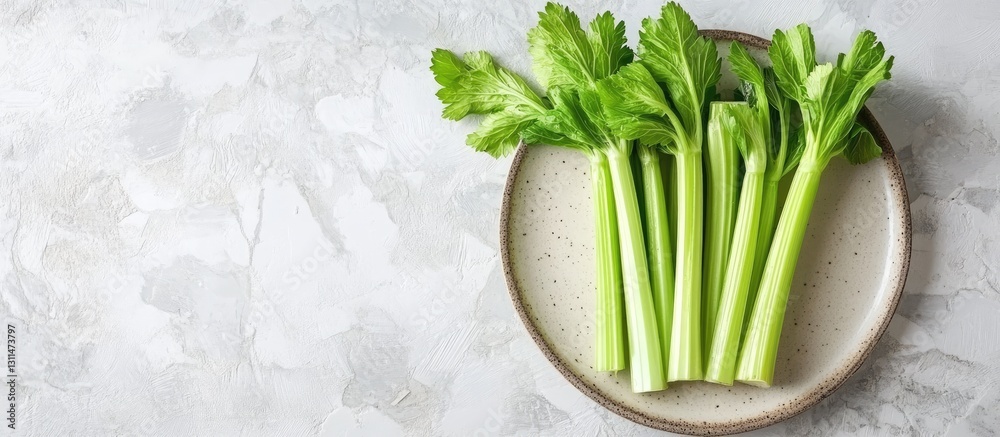 Poster fresh green celery stalks arranged neatly on a textured cream plate against a light stone background
