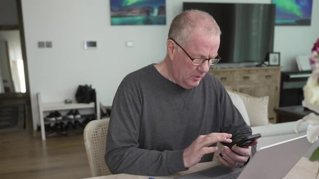 Older man on a smartphone and computer entering information from a form - sliding parallax