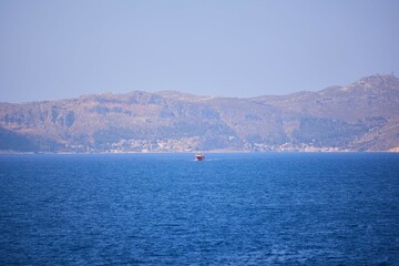 A ship or ferry sails across the Mediterranean Sea. In the distance is the Greek island of...