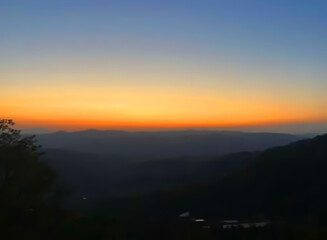 Beautiful sunset on the mountaintop, dazzling with bright orange and yellow colors painted on the sky, creating a peaceful twilight atmosphere.