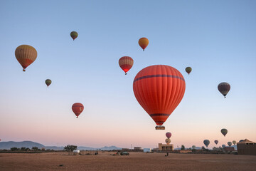 Hot air balloons float above an open landscape at sunrise, with mountains in the background. The...