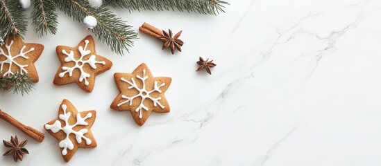 Decorative star-shaped Christmas cookies with icing surrounded by fir tree twigs and cinnamon sticks on a white marble table top viewed from above
