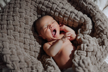 A baby is sleeping in a blanket. The blanket is brown and has a pattern of knots. The baby is making a grunting sound as it sleeps