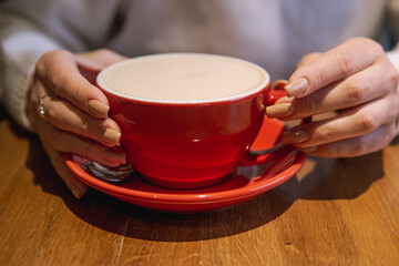 A cozy scene showing hands holding a red cup of a beverage on a wooden surface, highlighting a warm and inviting ambiance.
