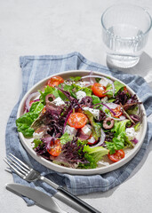 Vegetable salad (Greek salad) with cherry tomatoes, feta cheese, lettuce, olives and red onion in a plate