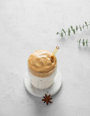 Korean whipped drink Dalgona coffee  on a marble stand on a light background with morning shadow.