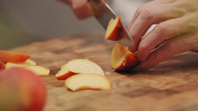 Koch bereitet Pfirsich zu auf Holzbrett mit Messer in K&uuml;che schneidet Obst mit H&auml;nden