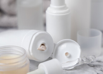 White cream tube with opened cap, pipette and bottles, beige scrub squeezing on table closeup