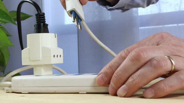 Cables connected to white power strip, man's hand inserts electrical cables into power strip in foreground.