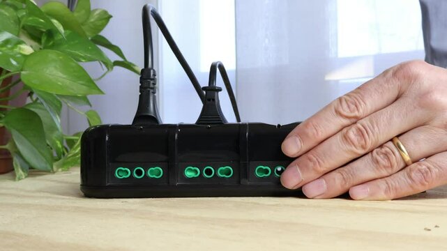 Cables connected to black power strip, man's hand removes electrical cables into power strip in foreground.