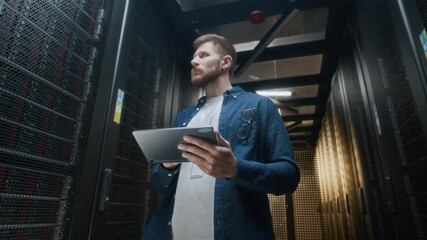 Zoom out low angle shout of young confident Caucasian male IT technician in casualwear inspecting rack server cabinets using digital tablet standing in server room in data center