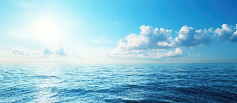 Serene ocean view featuring calm blue water under a bright sky with soft white clouds and sunlight reflecting on the surface on a clear day