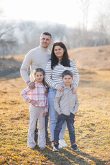 Fototapeta premium A family of four posing for a picture in a field. Scene is warm and happy, as the family members are smiling and hugging each other