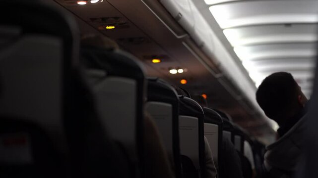 Focus on the ceiling of the passenger plane, where the safety elements, buttons and switches such as the oxygen mask are located. The man pulls himself up on the seat. High quality 4k footage
