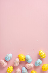 Decorated vertical Easter eggs in yellow, blue, and pink placed on a light pink background