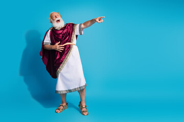 Full body photo of handsome senior male point empty space laughing wear ancient greek god king dress isolated on blue color background
