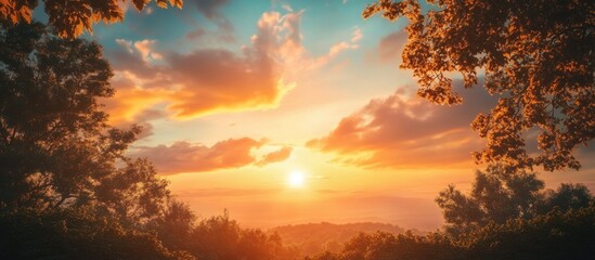 Obraz premium Vibrant sunset with orange and pink hues above lush green trees framed by clouds creating a serene landscape view in a tranquil nature setting
