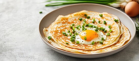 Thin crepes topped with egg and green onion on a light plate against a soft concrete background with ample copyspace for text integration